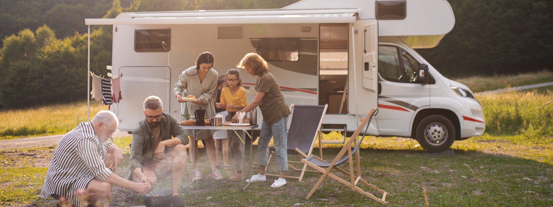 Familie som griller og setter frem mat foran en bobil.